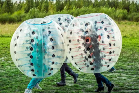 Tre personer i genomskinliga bubblor, redo för bumperball hyra. En rolig utomhusaktivitet med mycket skratt.