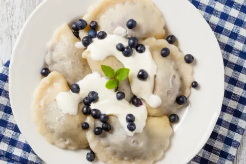Pyszne pierogi z jagodami, polane śmietaną i posypane świeżymi owocami. Idealne na letni deser.