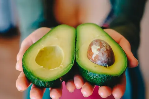 Manos sostienen un aguacate cortado por la mitad, listo para comer aguacate todos los días.