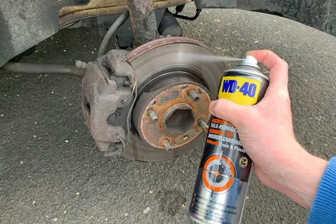 Hand sprüht Bremsenreiniger auf eine Bremsscheibe. Die Anwendung von Bremsenreiniger ist wichtig für die Wartung.