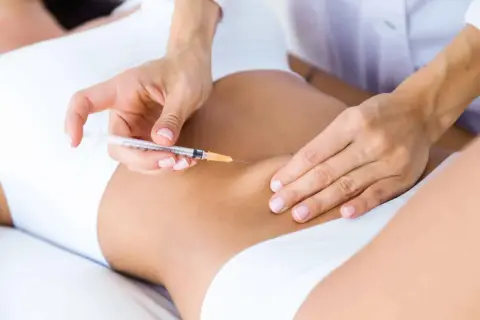 Manos expertas aplican carboxiterapia corporal con jeringa en la zona abdominal para mejorar la piel.