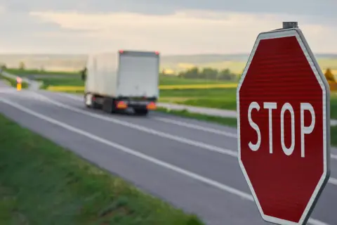 Czerwony znak stop na poboczu drogi, przed którym jedzie ciężarówka.