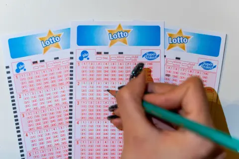 Ręka z ołówkiem zaznacza liczby na kuponach Lotto. Poznaj, jakimi metodami można zawierać zakłady gier liczbowych, wybierając swoje szczęśliwe cyfry.