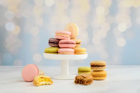 Bunte Macarons, frisch gebacken, stapeln sich auf einem weißen Tortenständer. Einige sind angeknabbert und zeigen ihre cremige Füllung.