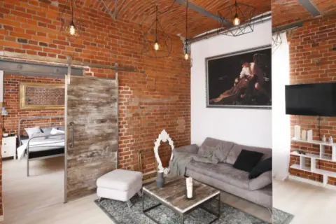 Nowoczesny salon z odsłoniętą, starą cegłą na ścianie. Wygodna sofa, stolik kawowy i przesuwne drzwi dodają charakteru.
