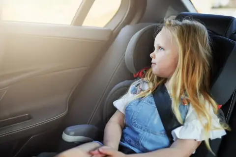 Ein blondes Mädchen sitzt im Kindersitz und schaut aus dem Fenster. Die Frage "wie lange Kindersitz" beschäftigt viele Eltern.