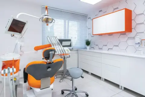 Nowoczesny gabinet stomatologiczny z fotelem dentystycznym w kolorze pomarańczowym i białymi meblami.