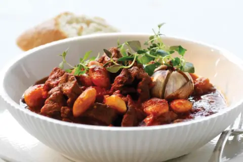 En skål med mustig chili con carne, garnerad med färska örter och en hel vitlöksklyfta. En bit bröd syns i bakgrunden.