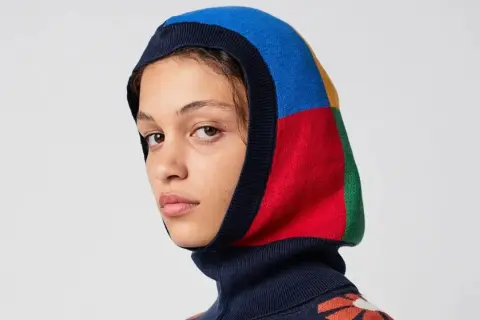 Mujer con balaclava que es una prenda de punto multicolor, con bloques de azul, rojo, amarillo y verde.