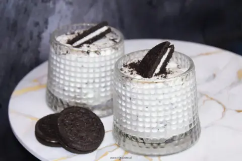 Dwa deserki z kremem i pokruszonymi oreo ciastkami, ozdobione połówkami ciastek.