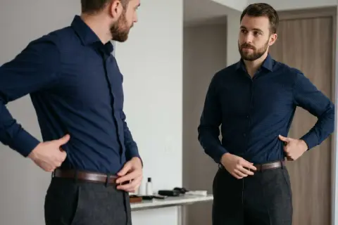 Mann steckt sein blaues Hemd richtig in die Hose, um einen gepflegten Look zu erzielen.