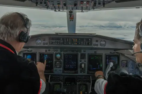 Dwóch pilotów w kokpicie, jeden wskazuje na ekran. Zastanawiasz się, ile zarabia pilot? To praca pełna odpowiedzialności.