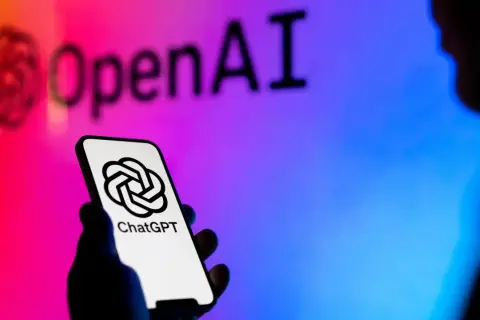 Dłoń trzyma smartfon z logo ChatGPT. W tle logo OpenAI, symbolizujące rozwój gpt sztuczna inteligencja.