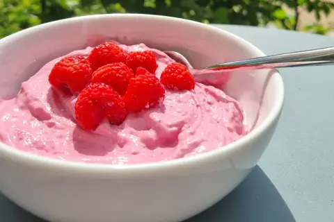 En skål med rosa krämig dessert toppad med färska hallon. Perfekt för nyttiga snacks en solig dag.