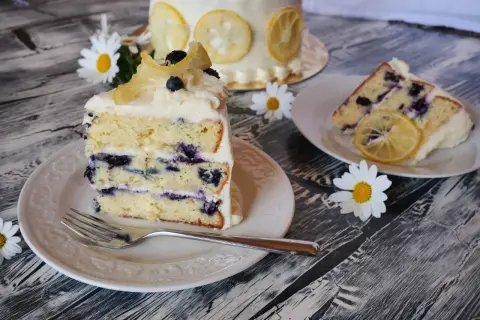 Ein Stück saftiger Zitronen-Blaubeerkuchen mit cremigem Frosting, garniert mit kandierten Zitronenscheiben und frischen Blaubeeren.