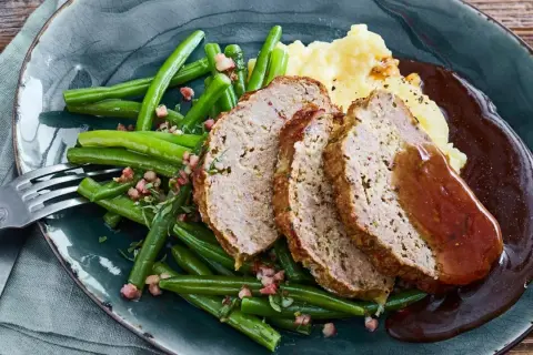 Saftiger hackbraten im ofen, serviert mit grünen Bohnen und Kartoffelpüree, übergossen mit dunkler Soße.