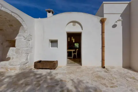 Interni di trulli pugliesi: un'apertura bianca rivela una sala da pranzo accogliente, con un camino e un piccolo orto in pietra all'esterno.