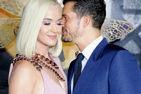 Orlando Bloom szepcze coś do ucha Katy Perry, która uśmiecha się z zamkniętymi oczami.