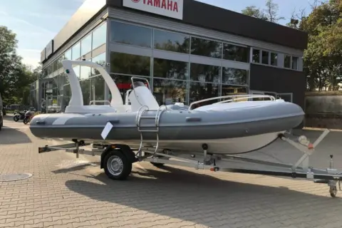 Szara łódź typu RIB na przyczepie przed budynkiem z logo Yamaha.