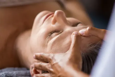 Mani esperte dimostrano come massaggiare il viso per le rughe, con un tocco delicato sulla fronte e sulle tempie per un effetto rilassante e ringiovanente.