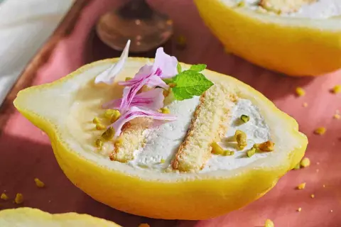 Delizia al limone: crema soffice e biscotti in un limone scavato, guarnito con pistacchi e petali rosa.