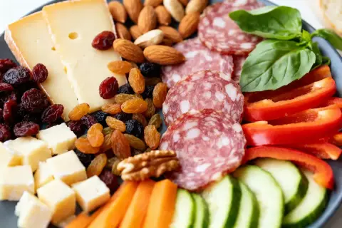 Une délicieuse planche apéro fromage avec salami, fruits secs, noix, poivrons rouges, concombres et carottes. Parfait pour un moment convivial.