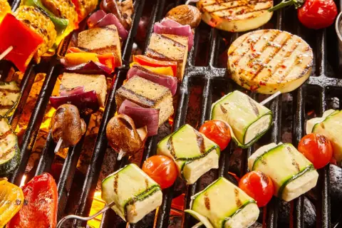 Bunte Spieße mit Tofu, Zucchini, Tomaten, Mais und Paprika brutzeln auf dem Grill. Ein Genuss für vegetarisches Grillen!