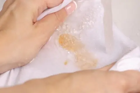 Hände waschen ein weißes Tuch mit Kaffeeflecken unter fließendem Wasser. So lassen sich Kaffeeflecken entfernen.