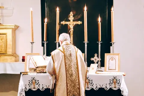 Kapłan w bogato zdobionej szacie odprawia mszę. Przed nim ołtarz z księgą i krzyżem. Świadectwo wiary, spowiedź powszechna.