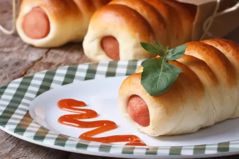 Leckere Bratwurst im Schlafrock, garniert mit einem Blatt, auf einem Teller mit Ketchup-Spur.