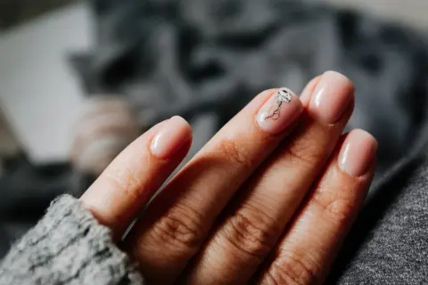Une main aux ongles rose pâle, avec une délicate méduse dessinée sur l'annulaire. Une manucure pastel subtile et élégante.