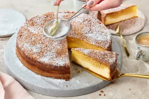 Ein köstlicher Kuchen mit Puderzucker wird bestäubt. Ein Stück wird mit einem goldenen Tortenheber herausgehoben. Dreh dich um, Kuchen, du siehst lecker aus!