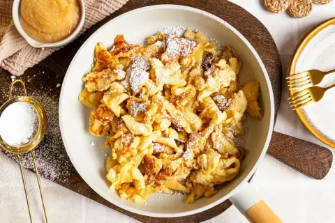 Kaiserschmarrn ohne Ei, fluffig und goldbraun, mit Puderzucker bestäubt. Dazu Apfelmus und zwei Gabeln.