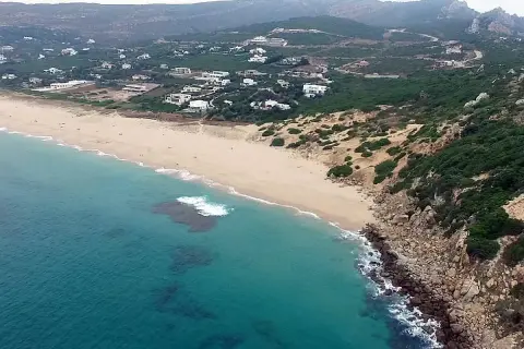 Vista aérea de la playa de los alemanes en Foz, con casas blancas dispersas entre la vegetación y el mar turquesa.
