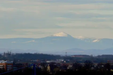 Widok na Śnieżkę i Karkonosze z Wrocławia. W oddali majaczą ośnieżone szczyty górskie, a na pierwszym planie widać zabudowania miejskie.