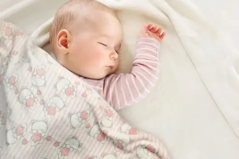 Śpiące dziecko otulone kocykiem w misie. Idealne wymiary kocyka dla niemowlaka zapewnią komfortowy sen.