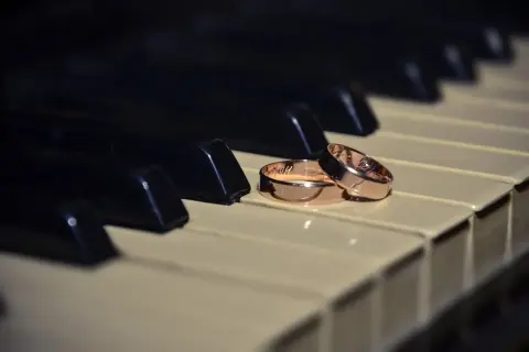 Dos alianzas de oro descansan sobre teclas de piano, evocando la pregunta: ¿cuanto pesa una alianza de oro?