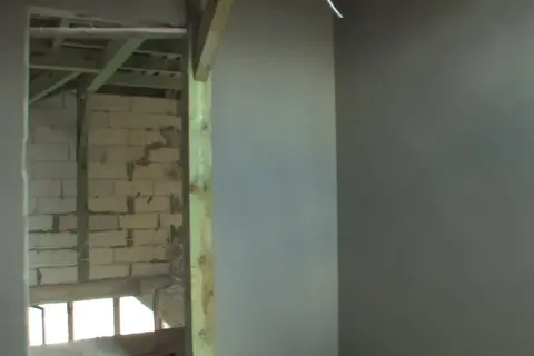 Ściana z tynkiem cementowo-wapiennym i widok na budowę w tle.