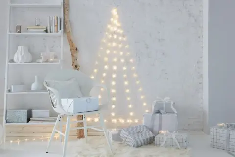 Eine Lichterkette an der Decke befestigt, bildet einen Weihnachtsbaum. Geschenke und ein Stuhl stehen davor.