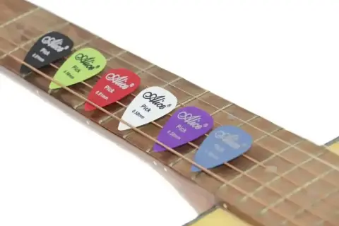 Kolorowe kostki do gry na gitarze Alice leżą na strunach. Każda kostka ma inny kolor i grubość.