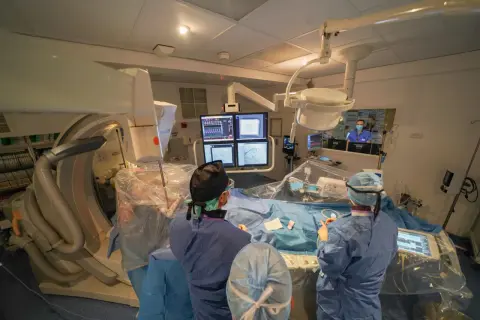 Équipe médicale en salle d'angiographie, préparant le repos après une coronarographie. Moniteurs affichant des images cardiaques.