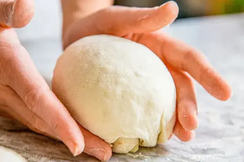 Hände formen einen Teigball auf einer bemehlten Oberfläche.