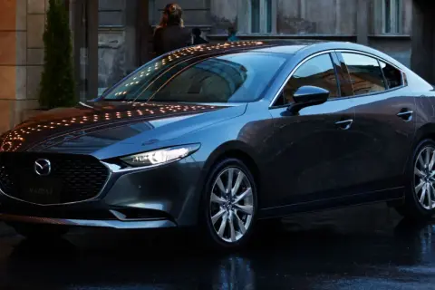 Elegancka, ciemnoszara Mazda 3 sedan stoi na mokrej ulicy, odbijając światła miasta.