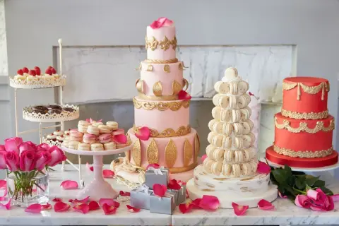 Ein prachtvolles Kuchenbuffet für eine Hochzeit: mehrstöckige Torten in Rosa und Rot, Macarons-Türme und Rosen.