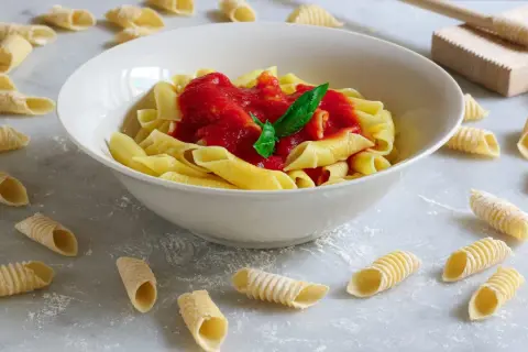 Garganelli alla contadina in una ciotola bianca, con pasta fresca sparsa sul piano di lavoro.
