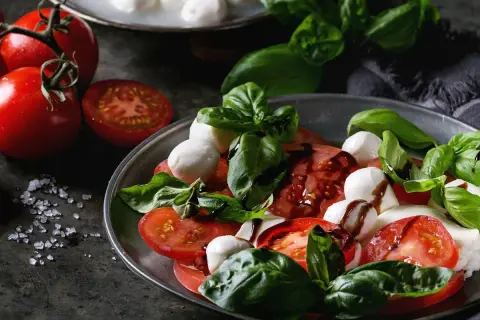 Sałatka caprese: soczyste pomidory, białe kulki mozzarelli i świeża bazylia, polane ciemnym sosem.