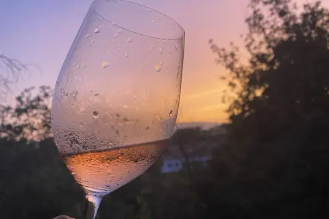 Calice di vino rosato, con gocce di condensa, al tramonto. Un brindisi alla vinificazione in rosato.