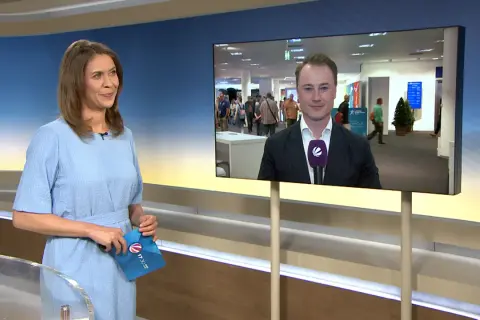 Moderatorin hält Umschlag mit Logo von tv-n hessen. Auf dem Bildschirm ein Reporter im Anzug.