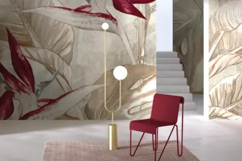 Egzotyczne, drogie tapety z motywem liści i kwiatów tworzą luksusową atmosferę. Czerwone krzesło i złota lampa dodają elegancji.
