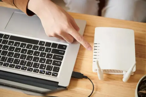 Ręka wskazuje na router, podłączony kablem USB do laptopa. Dowiedz się, jak połączyć falownik z wifi.